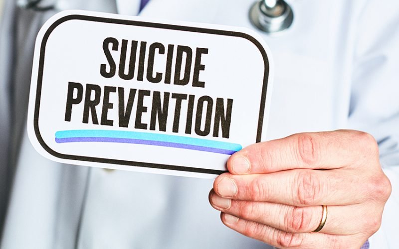 Unidentifiable male in a lab coat holding a medical sign: Suicide Prevention